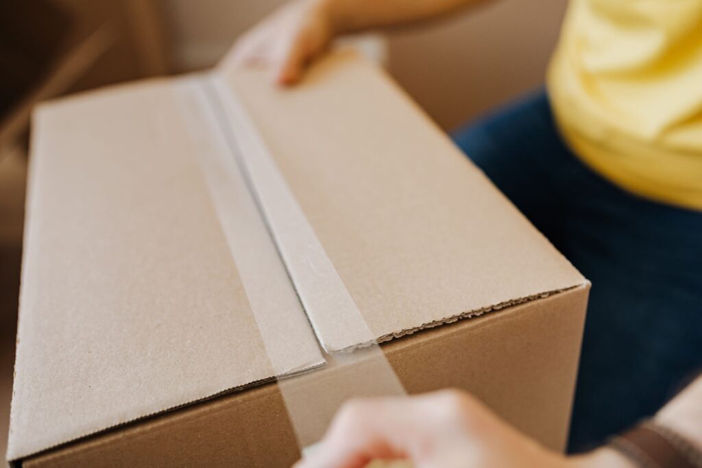 Person sealing a cardboard moving box with packing tape
